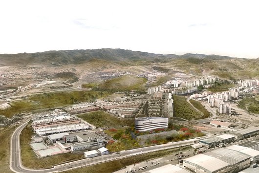 A town in a mountainous region with a large, modern residential complex in the foreground and hills in the background.