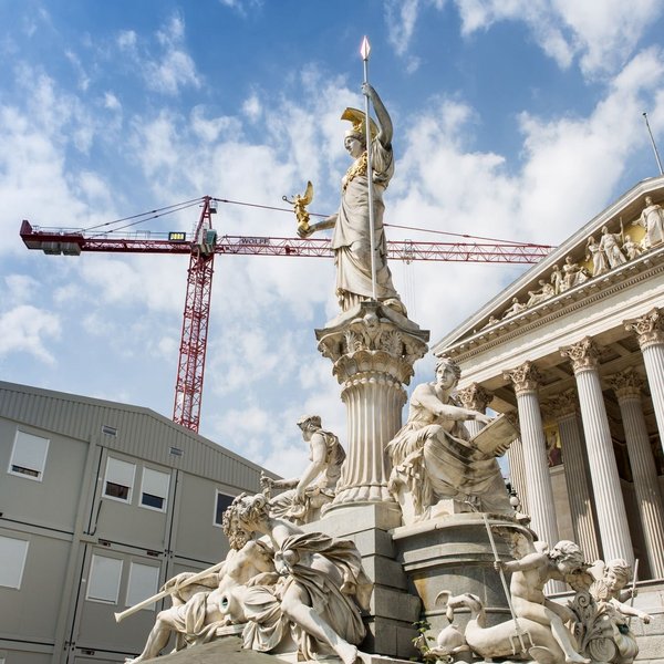 Österreichisches Parlamentsgebäude mit Statue im Vordergrund und Baucontainern sowie einem Kran links