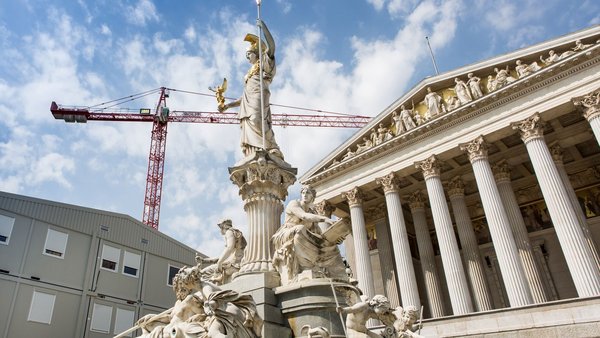 Österreichisches Parlamentsgebäude mit Statue im Vordergrund und Baucontainern sowie einem Kran links