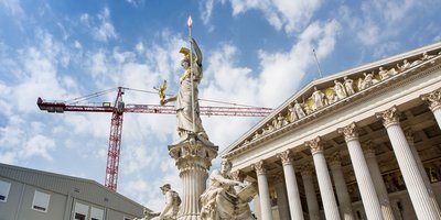 Österreichisches Parlamentsgebäude mit Statue im Vordergrund und Baucontainern sowie einem Kran links