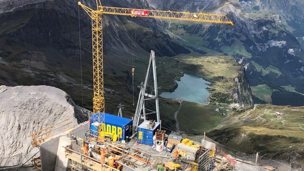 Construction site on the summit of a glacier with crane and view of a mountain lake and into the valley