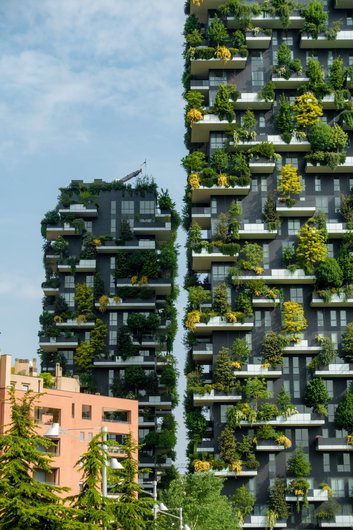 A section of the façade of the Bosco Verticale in Milan. The modern high-rise building is known for its numerous balconies, which are planted with lush plants and trees.