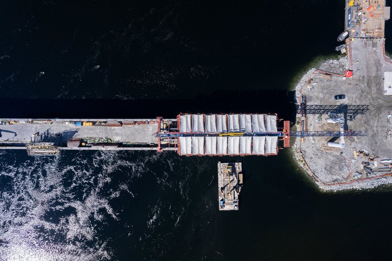 An aerial view of a construction site on a river or canal where a bridge structure is being built.