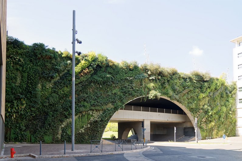 Ein bepflanztes Viadukt in der Stadt, vollständig mit üppiger Vegetation bedeckt. Die Begrünung erstreckt sich über die Bögen und Seiten und verbessert die Luftqualität und das Mikroklima.