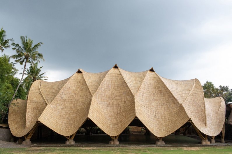 A large bamboo building with a corrugated roof construction and open sides.