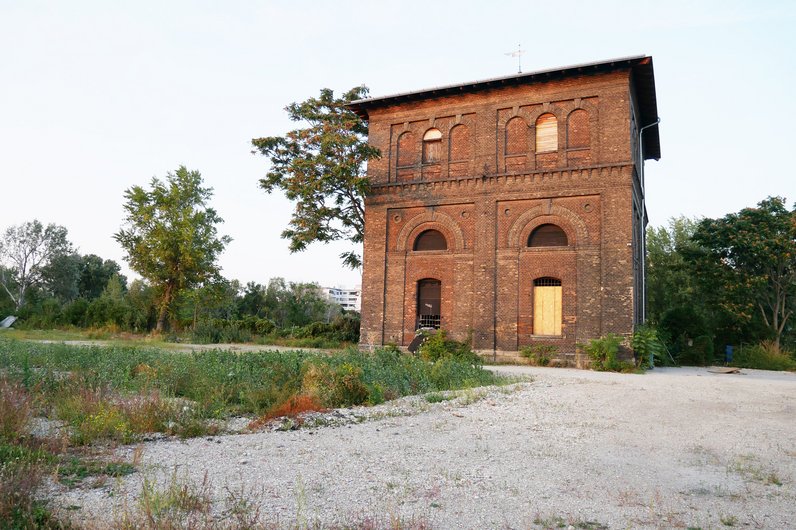 A two-storey, old brick building in a rural setting with trees and grassy areas.