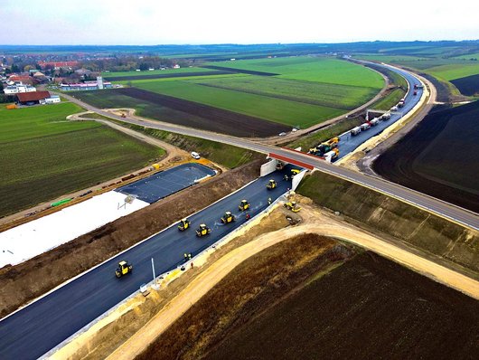 Aerial view of a road construction site where several machines are working on a newly asphalted road.