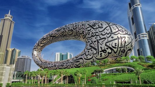 Oval museum building with palm trees in the foreground and skyscrapers in the background