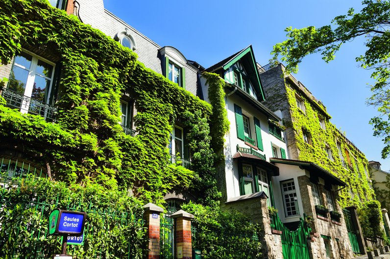 A picturesque street in Montmartre, Paris, with houses whose façades are covered in green climbing plants.