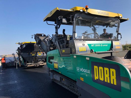 Road construction machines from PORR and Vögele are used to asphalt a road.