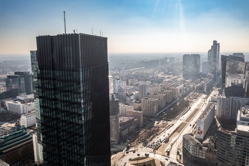 Eine Stadtlandschaft mit einem großen, modernen Wolkenkratzer im Vordergrund und einer breiten Hauptstraße, die durch die Stadt verläuft.