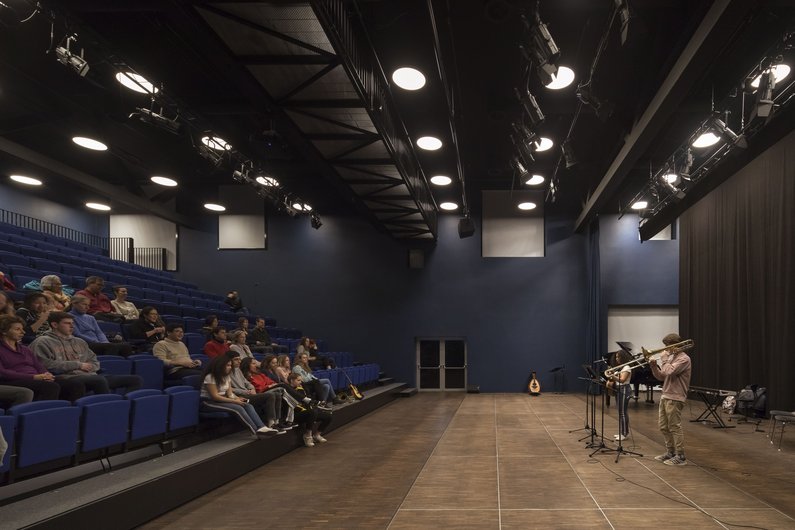 A modern performance space with blue seats, in which two musicians stand on the stage.