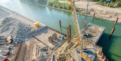 Aerial view of a construction site on a riverbank with a large crane and various building materials.