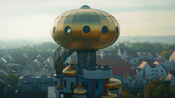 Drone shot of a colourful tower with a golden sphere at the top, city in the background