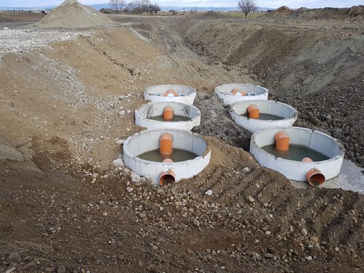 Several round concrete containers with orange-coloured pipes are installed in an excavation pit.