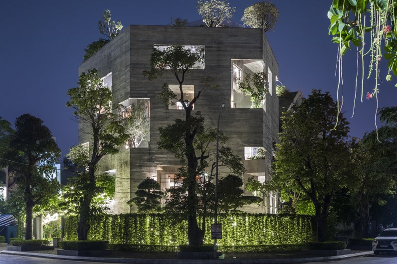 A modern building at night, surrounded by plants. Illuminated windows and balconies are interspersed with trees and shrubs, creating a harmonious atmosphere.