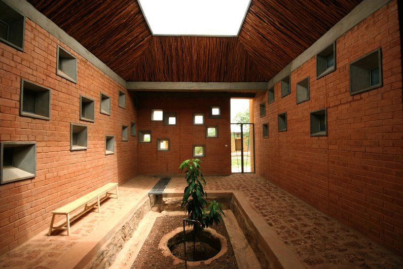 The interior of a building designed by Francis Kéré with brick walls, a natural roof and a central light window.