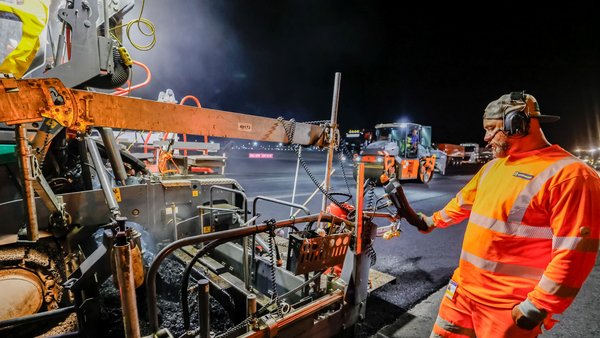 Construction workers renovating a taxiway at the airport at night.