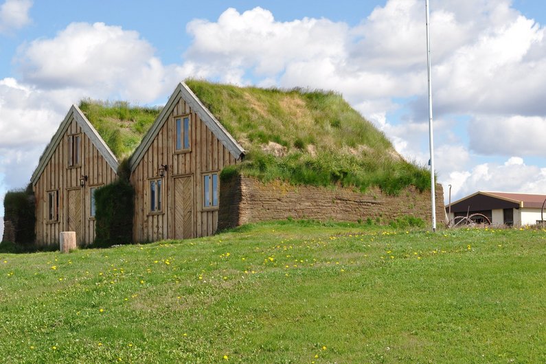 Two traditional wooden houses with grassy roofs in a green, open landscape.