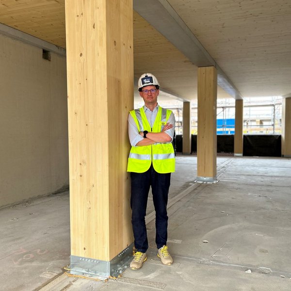 Mann mit Helm lehnt an einer Holzstütze auf einer Baustelle