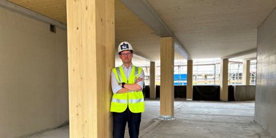 Mann mit Helm lehnt an einer Holzstütze auf einer Baustelle