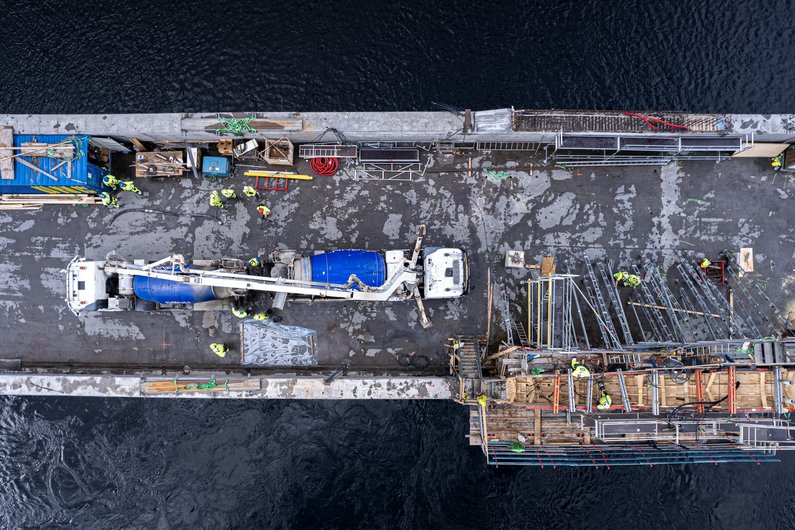 Aerial view of a construction site on a waterway, showing a concrete mixer and several construction workers.