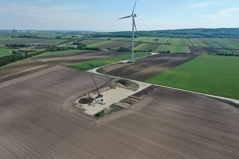 A large wind turbine on an extensive field with green and brown plots.