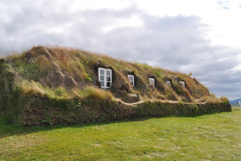 A traditional Icelandic turf house whose roof and walls are overgrown with grass and moss.