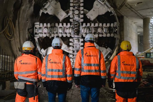 Vier Männer von hinten vor einer Tunnelvortriebsmaschine
