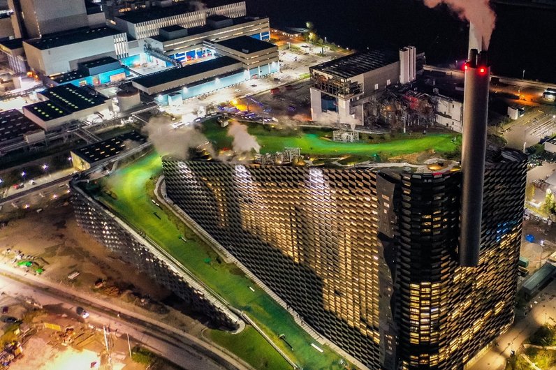 A night-time aerial view shows a modern, illuminated building with a green roof.