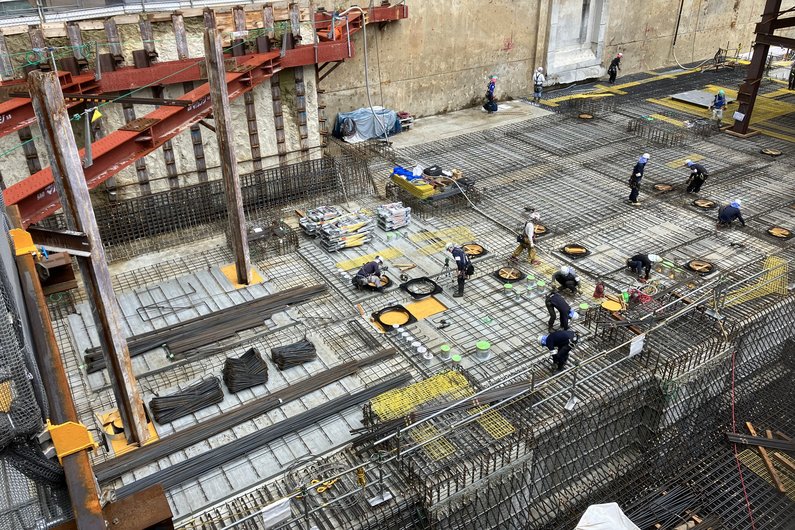 Eine Baustelle, auf der Arbeiter an der Bewehrung für eine Betonfundamentplatte arbeiten.