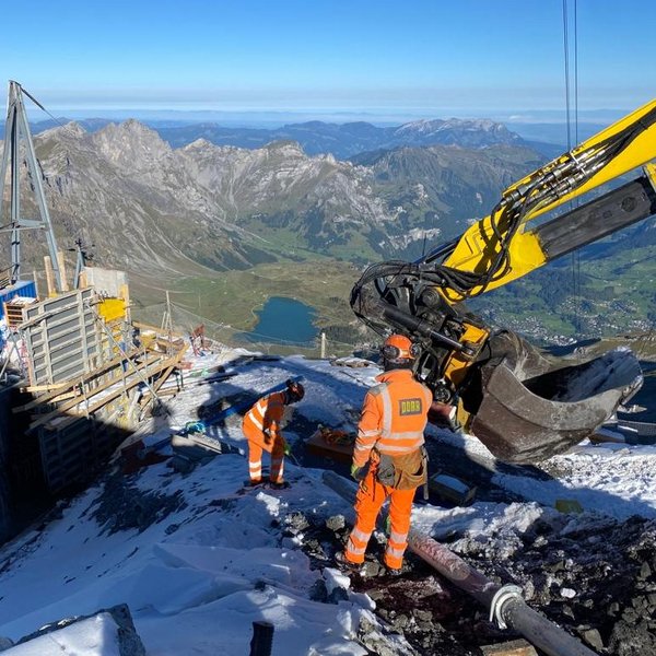 Baustelle auf dem Gipfel eines Gletschers mit Bagger und Blick  auf einen Bergsee und ins Tal