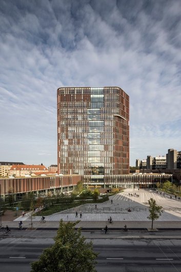 A modern high-rise building with a glass and brick façade, surrounded by a large square and urban surroundings.