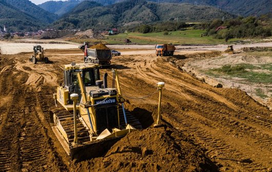 A construction site in a hilly landscape with several excavators and lorries.