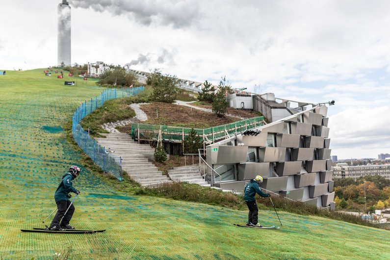 Two skiers on a green, artificial slope.