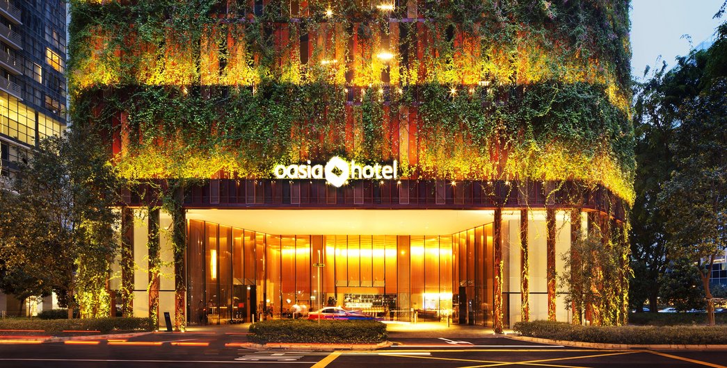 The Oasia Hotel in Singapore with an impressive green façade that is illuminated at night.