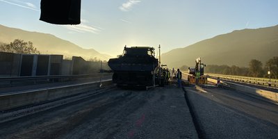 Eine Straßenbaustelle bei Sonnenaufgang, umgeben von Bergen und klarem Himmel.