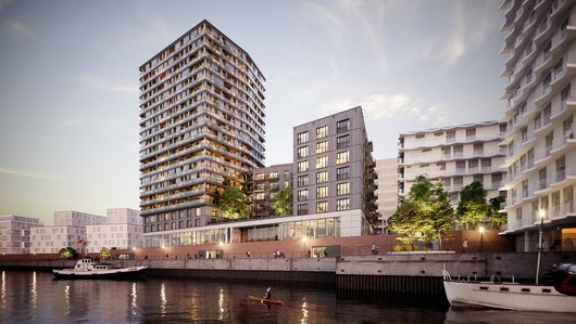 Modern residential buildings on a riverbank, including a tall tower and lower, green structures.