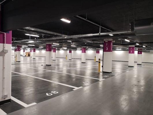 A modern, well-lit underground car park with numbered spaces and purple columns.